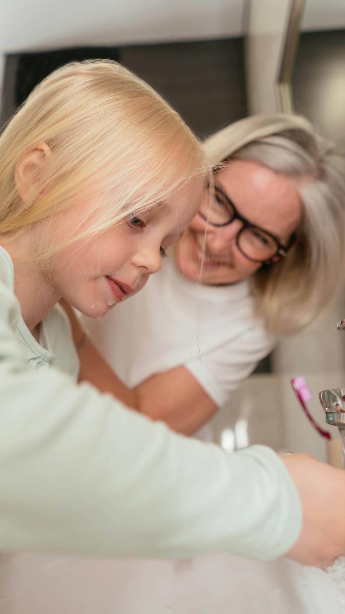 A woman and young girl washing hands, focusing on family bonding and hygiene.